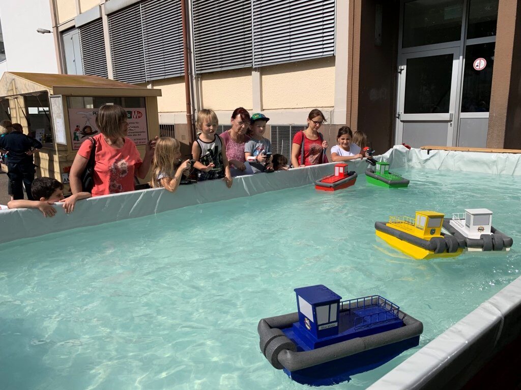 Kinder beobachten bunte Modellboote in einem Wasserbecken während einer Veranstaltung zum Schiffsmodellbau.