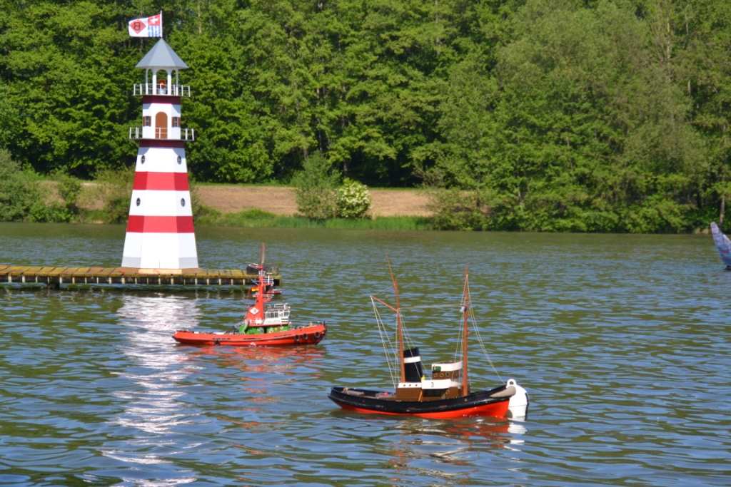 Zwei Schiffsmodelle fahren auf dem See von Courtavon, mit einem Leuchtturm im Hintergrund.