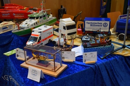 Modellschiffe und Fahrzeuge auf einem Tisch, darunter Rettungsboote und ein Lkw, umgeben von blauer Tischdecke.