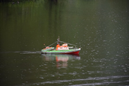 Ein detailliertes Schiffsmodell fährt über einen ruhigen See bei Regen, in leuchtenden Farben gestaltet.