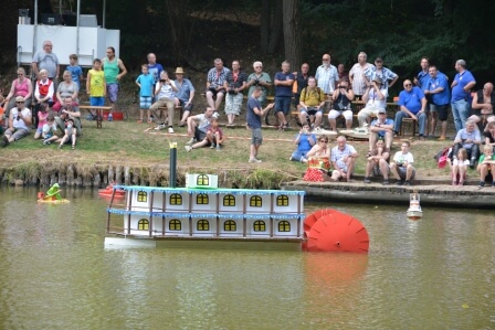 Ein Modell eines Raddampfers schwimmt auf dem Wasser, umgeben von Zuschauern am Ufer in Pirmasens.