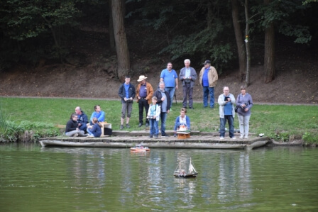 Gruppierung von Modellbauern am Teich, die Schiffsmodelle steuern und beobachten.